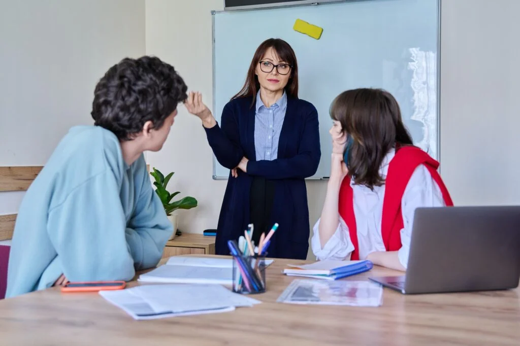 Middle aged female teacher giving lesson to teenage college students sitting at table
